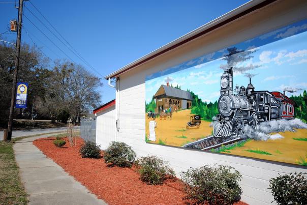 A mural of a steam engine train chugging through the countryside painted on the side of a Hope Mills, NC building