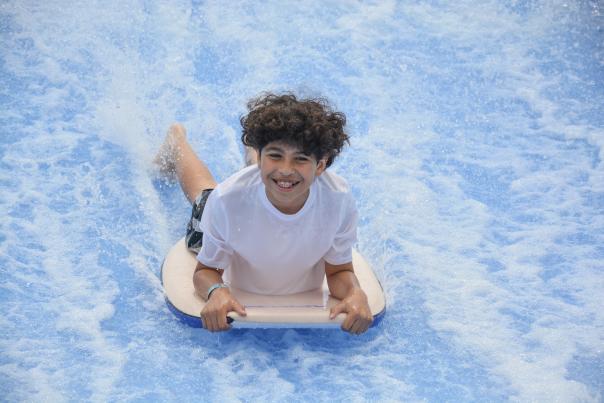 A boy surfing on his stomach at RIVERPSORT's Summer Camp