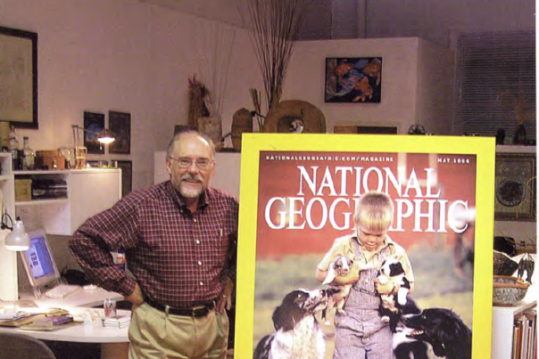 a man stand next to a large cover of a magazine with a young boy surrounded by dogs on it