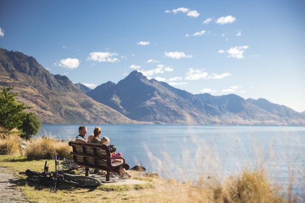 Family sitting on bench along the Queenstown Garden's Trail overlooking mountains