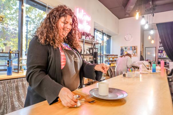 An image of Scents By Design's female owner making a custom candle at the shop.