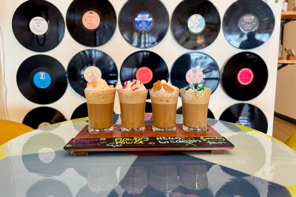 A wooden tray sitting on top of a table with four different flavored ice lattes on it at Jinkies! Coffee & Hangout