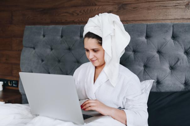 A woman in a robe works on a laptop in a bed