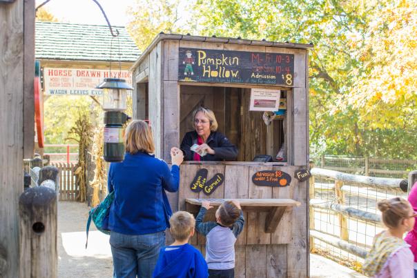 Family of three stands in front of the wooden check-in booth at Deanna Rose Children's Farmstead