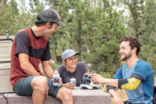 Three friends sitting around a park bench having a beer after biking together.