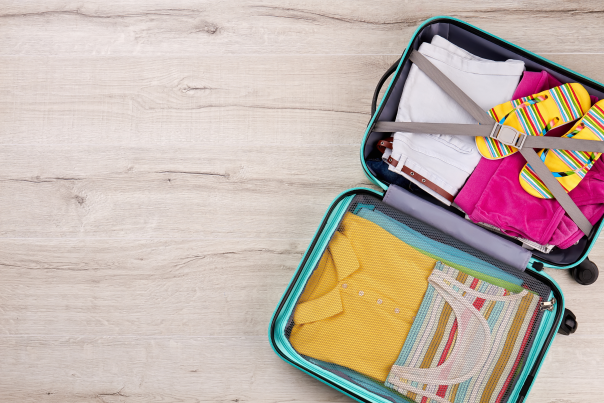 An open suitcase with colorful beachwear inside sits on a light wooden background