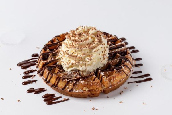 A waffle drizzled with chocolate syrup and topped with whipped cream