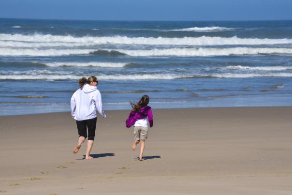 A woman and young girl run towards the waves on the beach.