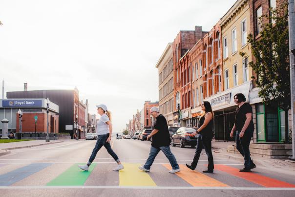 People walking across a crosswalk with pride colours.
