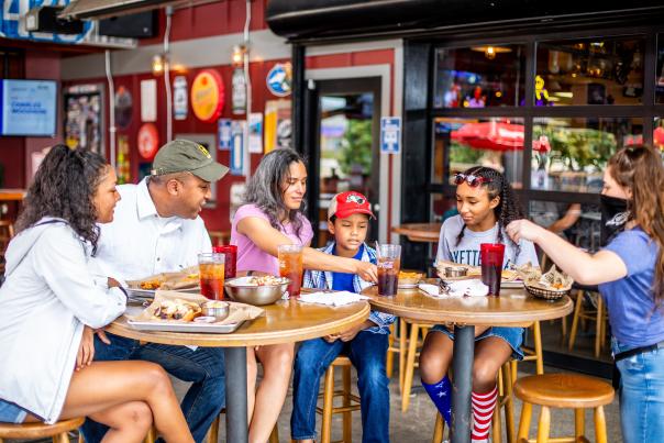Family and friends gathered around an outdoor restaurant table sharing food and drinks together