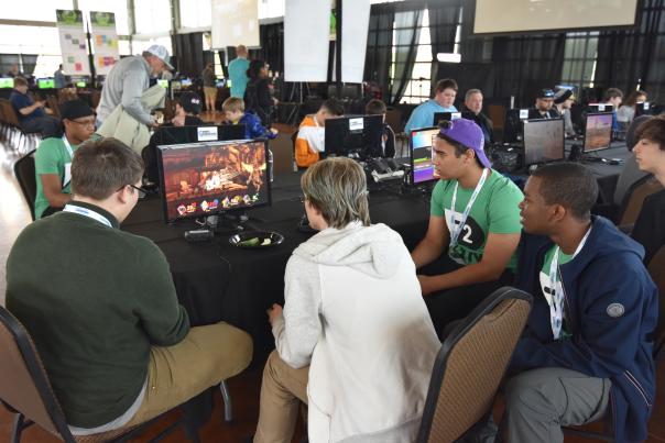 a group of guys around a computer game in a large venue
