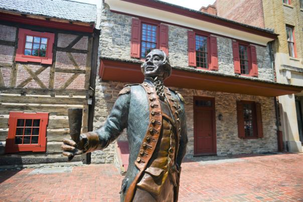 Historic statue of a colonial man outside of a two-story, stone building