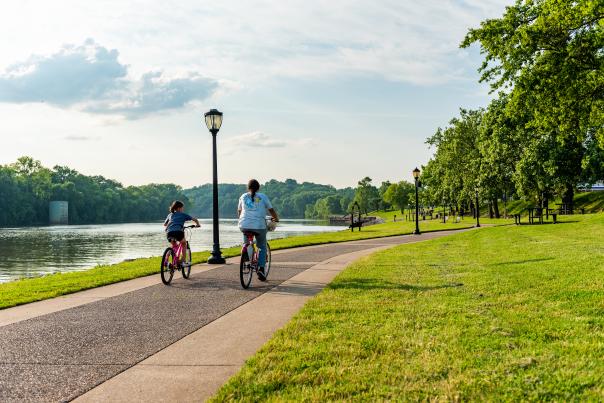 two girls ride bikes along a paved path next to a river