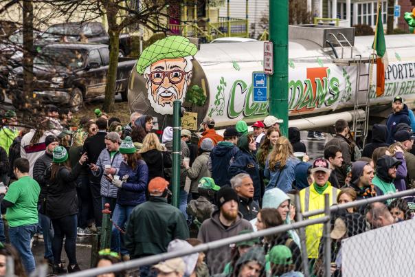 A tank full of green beer with a giant picture of a man's face on the back surrounded by a crowd
