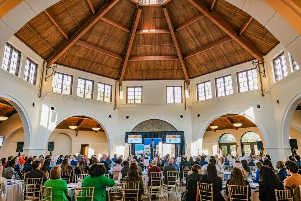 Conference attendees seated inside the Cape Fear Botanical Garden event hall in Fayetteville, NC, listening to a speaker under the vaulted wooden ceiling.