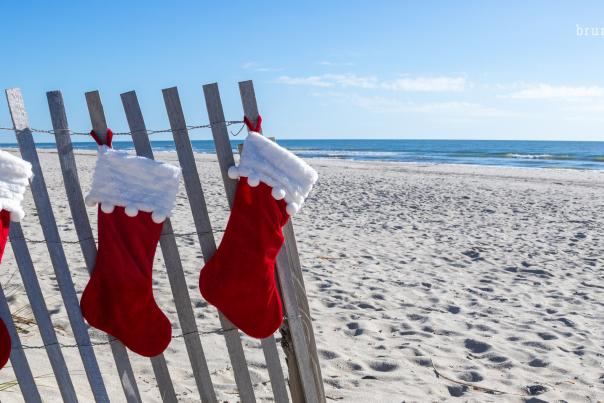 3 red Christmas stockings hanging from sand fence on the beach