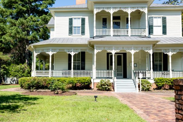 Front view of the historic 1897 Poe House in Fayetteville, North Carolina, surrounded by greenery and featuring its signature wraparound porch and ornate trim.