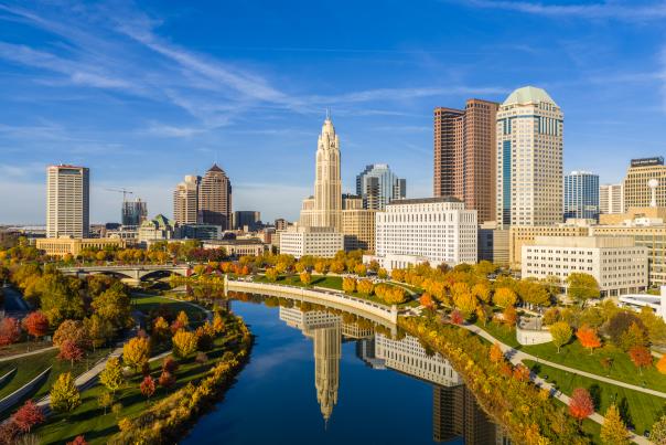 Columbus skyline reflecting in the Scioto River, with red and orange trees lining the river