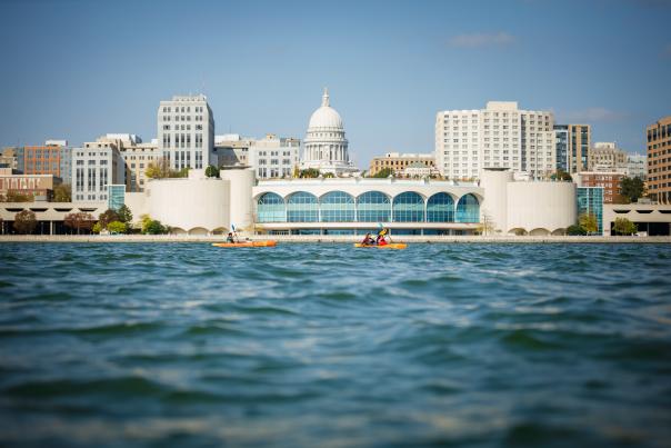 A wide shot of a family kayaking on lake Monona in front of Monona Terrace with the Madison skyline in the background