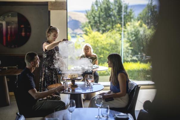 Waitress serving guests at Amisfield Restaurant, lifting up a lid of a dish with smoke coming up