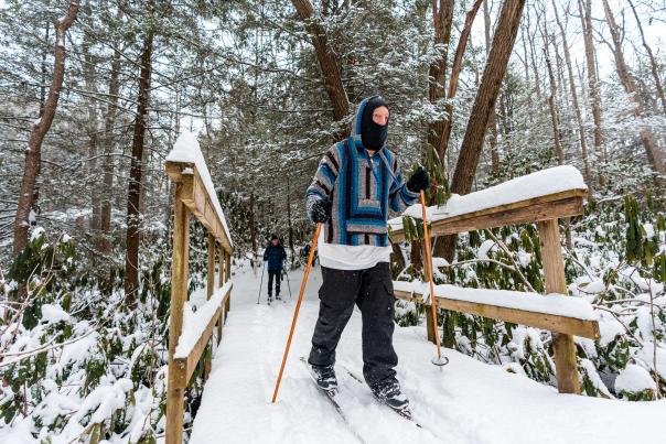 Two people in winter gear cross country skiing across a snow-covered, wooden bridge in the Laurel Highlands