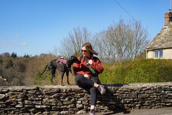 Lottie Gross with her dog sat on a Cotswold stone wall