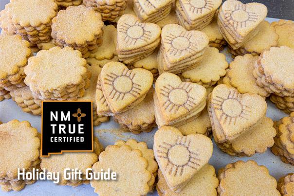 Assortment of heart-shaped cookies, some with embossed designs, displayed on a counter. "NM TRUE CERTIFIED" logo visible in the corner with text "Holiday Gift Guide" below.
