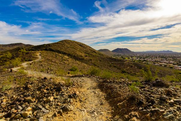 Trail through a desert landscape with mountains and city in the background