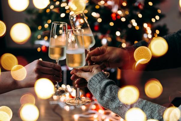 A group of people clink champagne flutes surrounded by twinkling Christmas lights