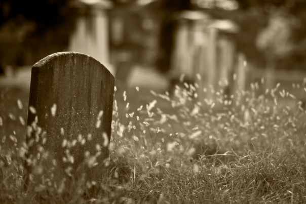 sepia image of gravestone in foreground of graveyard