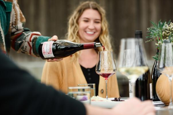 Red wine is poured into a glass with a smiling person watching.