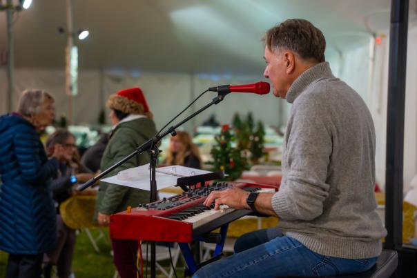 Musician playing keyboard and singing into a microphone at a holiday event