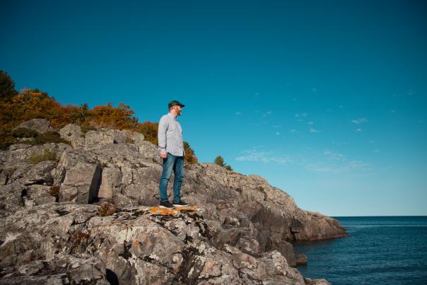 A man standing on rocks on the shore of Lake Superior on a sunny, fall day.