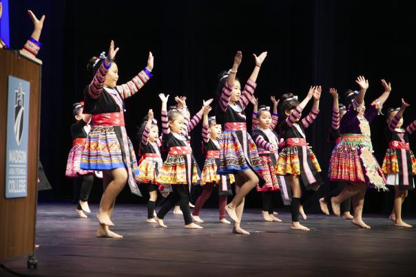 A group of Hmong girls dance on stage in traditional dresses during a Hmong New Year celebration