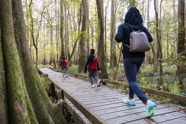 Two kids and a mother jog down a boardwalk through the woods