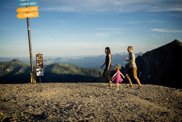 A happy family hiking on top of a mountain with ski trail sign markings