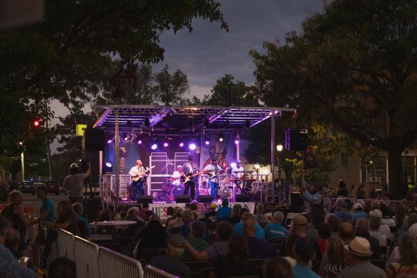 A blues band performing on an outdoor stage at Michigan BluesFest, with guitars, drums, and a cheering crowd.