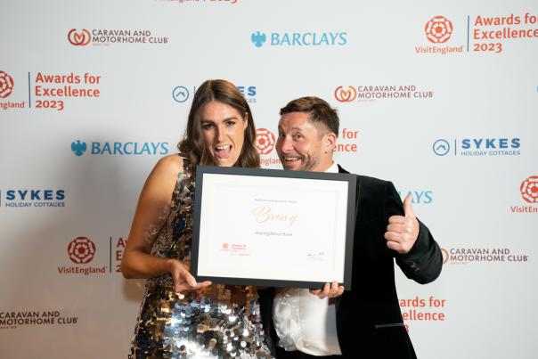 A man and a woman hold a certificate that reads 'bronze' in front of a Visit England press board at a celebration event