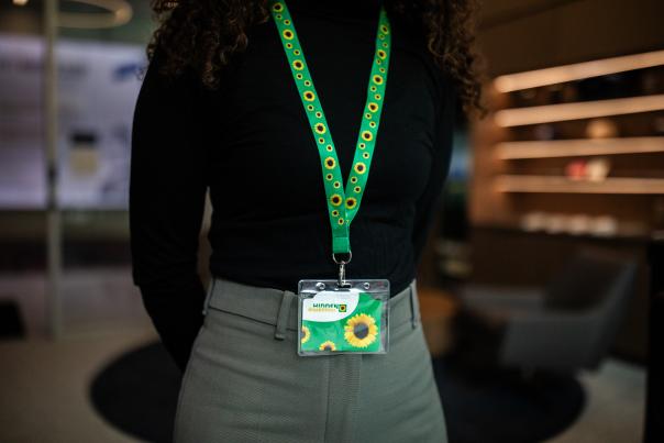 a person wears a sunflower-patterned Hidden Disability Sunflower lanyard with a badge over a black shirt and grey slacks
