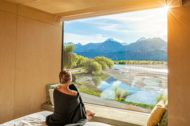 Woman looking out a huge window with view of mountains and lake at Kinloch Wilderness Retreat