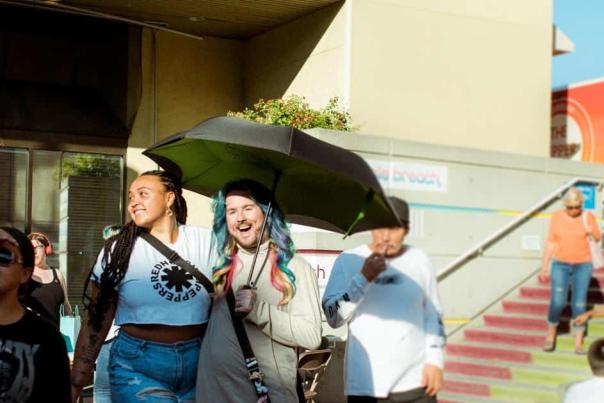 Two people walking under an umbrella in the sun.