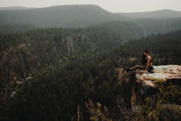 Girl sitting on cliff overlooking rolling hills of pine trees