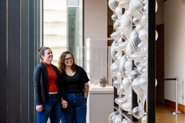 A couple holding hands looking at a glass art piece at the Chazen Museum of Art