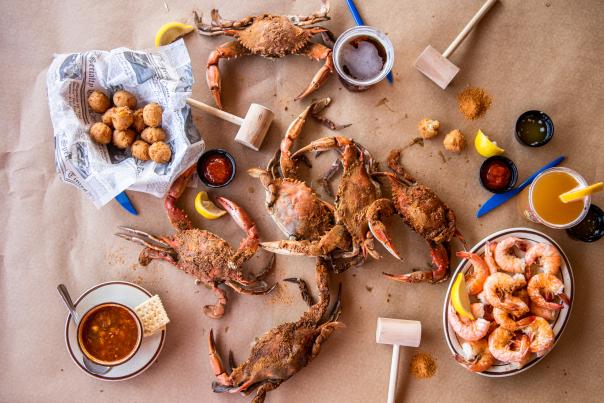 A brown parchment lined table with mallets and steamed crabs, shrimp and hushpuppies on the table.
