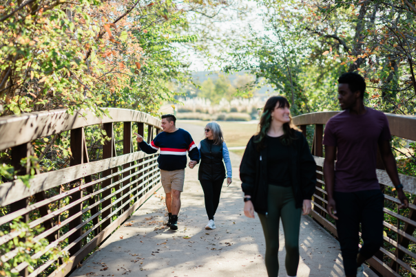 Two couples walking along a bridge looking at the greenery in the park