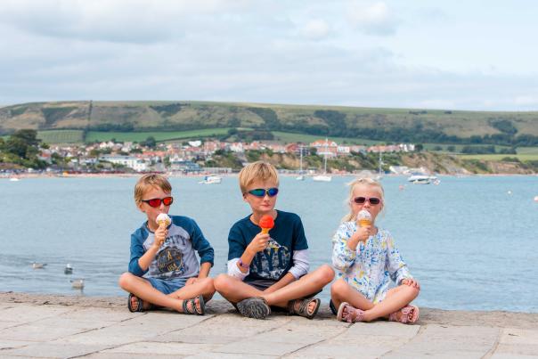Three children eating ice cream in front of Swanage Bay Dorset