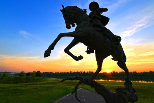 A bronze statue of a man riding a rearing horse is back lit by the setting sun at the U.S. Marshalls Museum in Fort Smith, Arkansas.