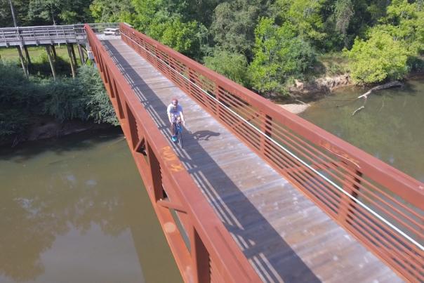 Drone Shot of Man Cycling on a Bridge Over a River