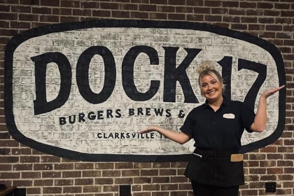waitress poses with arms up beside Dock 17 logo