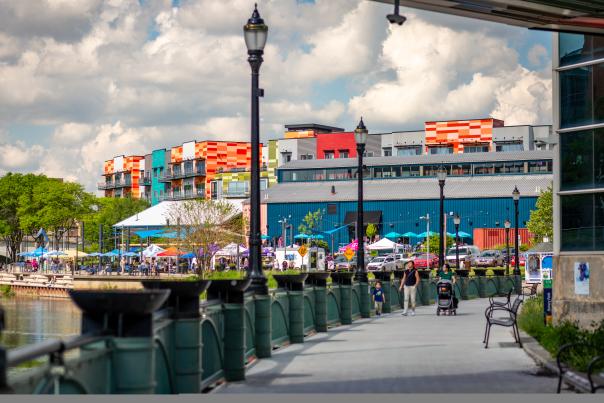 Scenic view of the Lansing River Trail near Rotary Park and Lansing Shuffle, showcasing the riverfront pathway, lush greenery, and outdoor dining spots. The vibrant atmosphere invites visitors to explore, relax, and enjoy the beauty of Lansing’s waterfront.